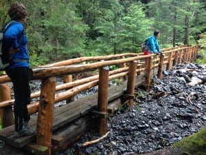 Hikers on the Herring Cove Trail footbridge. Flood waters pushed rocks under most of the span, turning it into a dam. (KCAW photo/Robert Woolsey)
