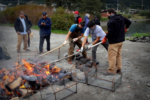 Carvers rake back the embers to reveal the heated lava rocks, which they'll shovel into the metal baskets. (KCAW Photo/Emily Russell)
