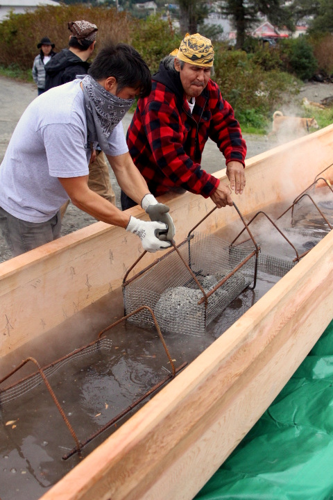 Jerrod Galanin gets help lowering a basket of hot lava rocks into the canoe. (KCAW Photo/Emily Russell)