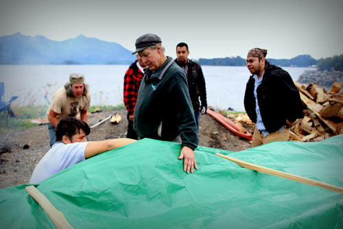 Master carver Steve Brown oversaw the steaming, while Jerrod Galanin takes a look under the tarp. (KCAW Photo/Emily Russell)