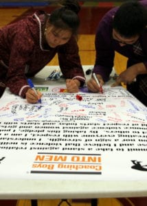 Two student wrestlers sign the poster after completing the 'Coaching Boys into Men' program. (Emily Russell/KCAW)