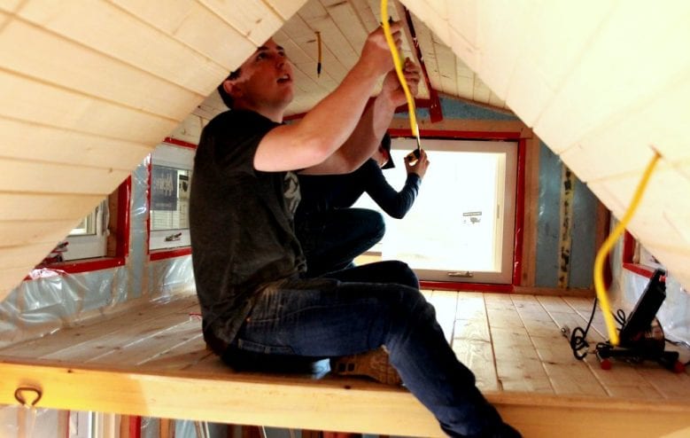 Sitka High senior Jackson McGraw stretches a measuring tape for fellow senior Kyler Sumauang along the ridge of the tiny home. (KCAW photo/Robert Woolsey)