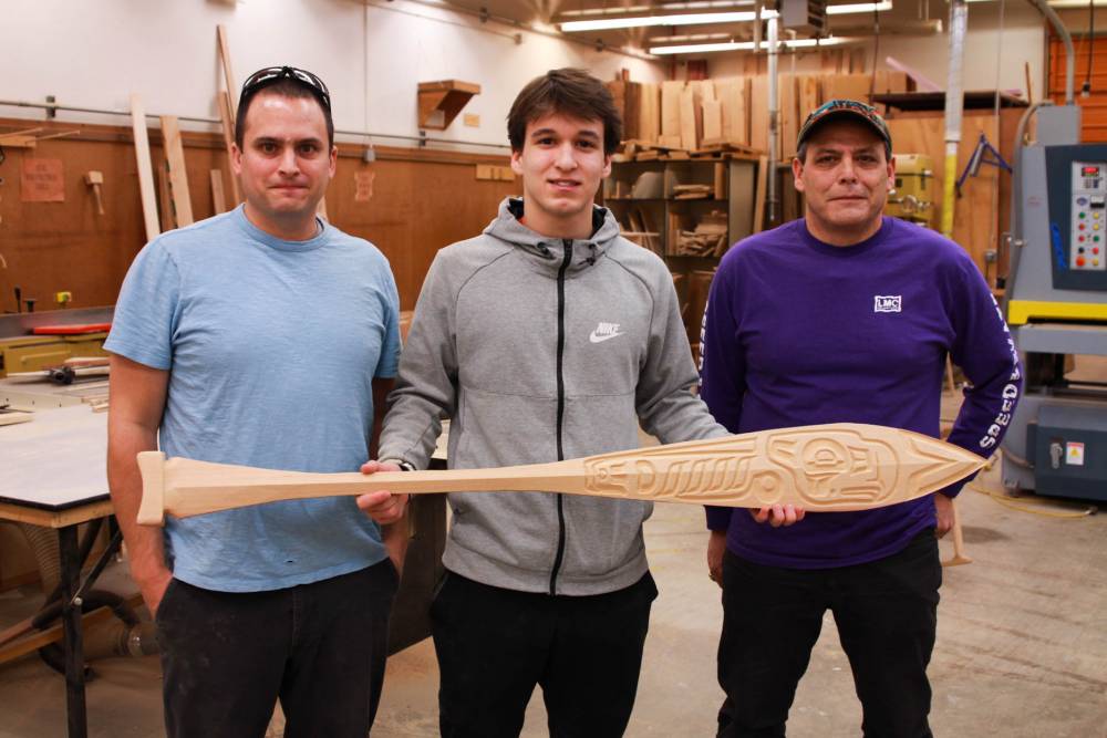 Sitka High School junior Asa Demmert, center, shows off his nearly-finished paddle featuring an eagle alongside Sitka High design instructor Mike Vieira, left, and STA traditional arts instructor, Charlie Skultka, right. (KCAW Photo / Enrique Pérez de la Rosa)